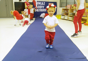 Miłosz ubrany na biało czerwono pozuje podczas "Pokazu mody patriotycznej" na granatowym dywanie.